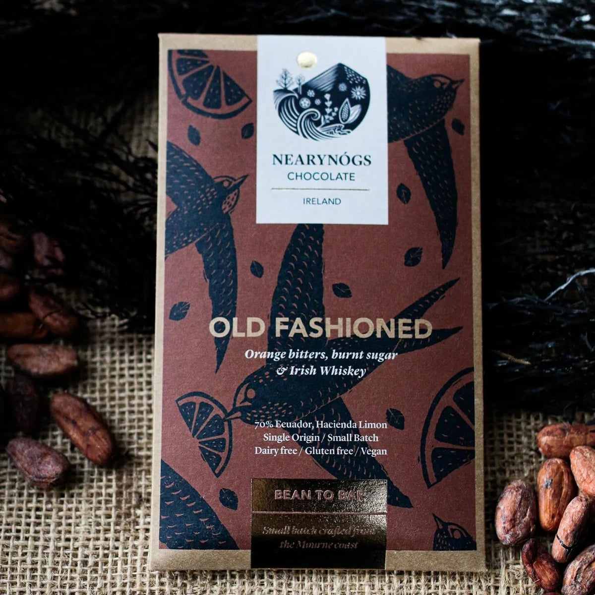 A package of Nearynógs Chocolate 'Old Fashioned' chocolate bar, styled on a burlap surface with cocoa beans.