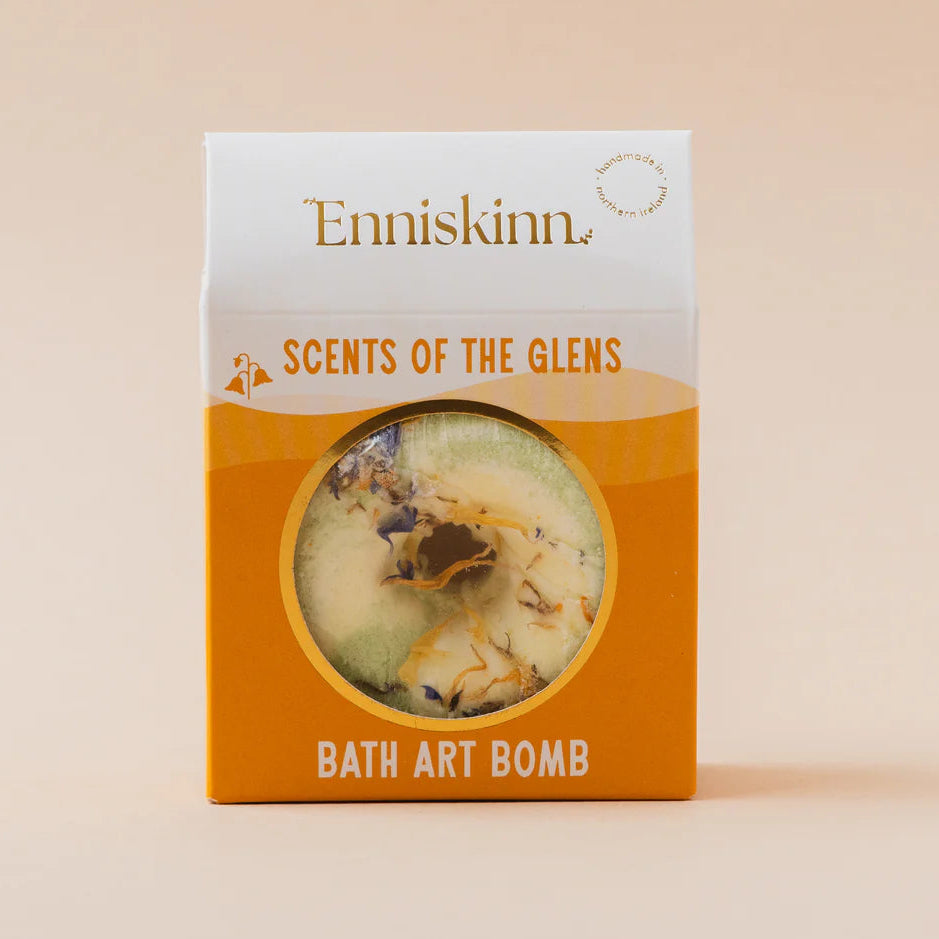 Enniskinn 'Scents of the Glens' Bath Art Bomb in its retail packaging, featuring a white and orange box with a circular window showing the bath bomb inside.