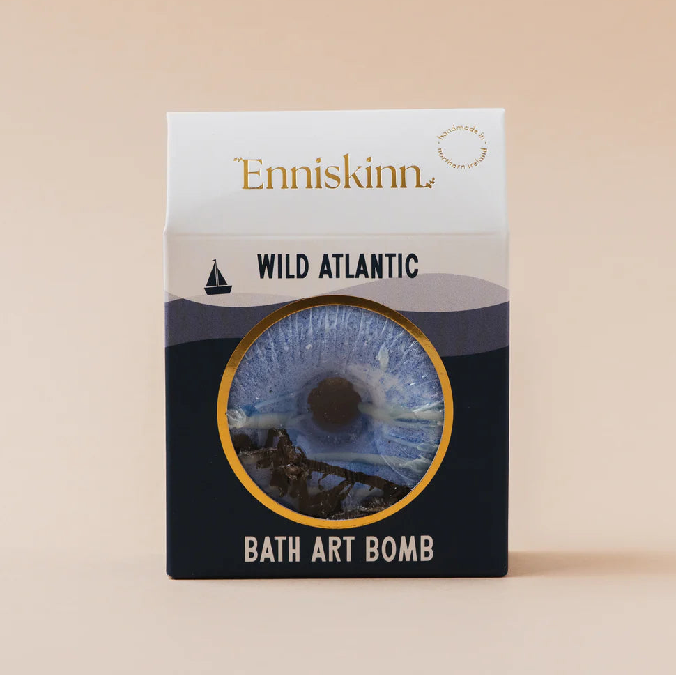 Enniskinn Wild Atlantic Bath Art Bomb in its packaging, featuring a dark greyish blue design with a circular window showing the blue bath bomb inside.