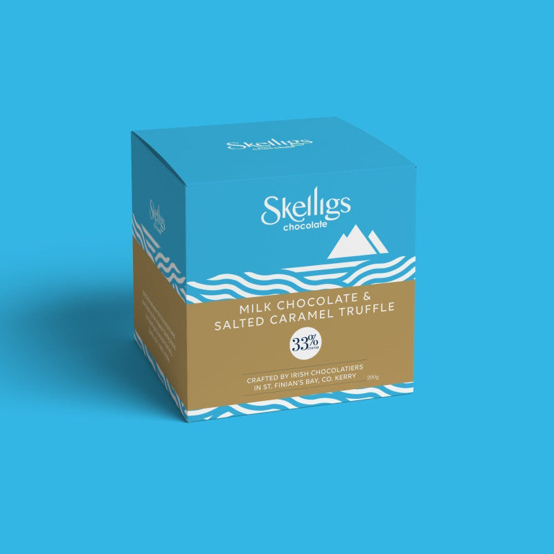 A square product box for Skelligs Chocolate 'Milk Chocolate & Salted Caramel Truffle' on a solid blue background. The box features a blue top half with white wave details and a tan bottom half with white text.