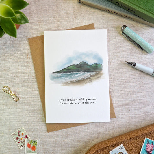 A white greeting card with a watercolor mourne-mountains-and-sea illustration and the printed phrase 'Fresh breeze, crashing waves, the mountains meet the sea'.